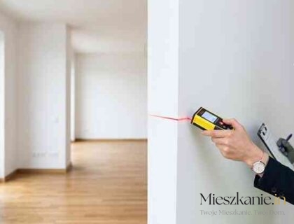 Inżynier w białym kasku i kamizelce odblaskowej wykonuje pomiar ściany dalmierzem laserowym w nowym, pustym mieszkaniu w stanie deweloperskim.